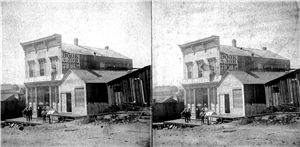 Men stand on the front porch of a late 19th century two story building with a marquee that says Intelligencer. One man is standing on top of the marquee outside a second story window